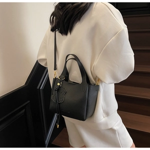 Detail of black lychee grain leather bucket bag featuring a cute bear bag charm accessory