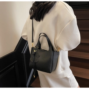 Close-up of black pebbled leather bucket bag with cute bear charm and shoulder strap