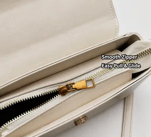Detail view of smooth golden metal zipper and fine stitching on the cream leather handbag