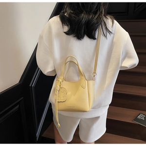 Detail of creamy yellow lychee leather bucket bag with cute bear charm and gold logo
