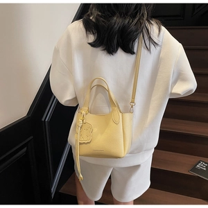 Detail of cream yellow bucket bag with bear charm worn by model in casual white outfit