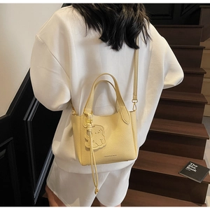 Detail view of yellow lychee grain bucket bag with cute bear charm worn on back
