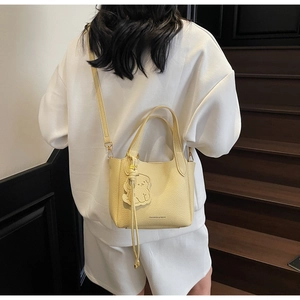 Close-up of creamy yellow bucket bag with lychee texture and cute dog charm on stairs