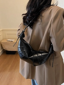 Glossy black croissant shoulder bag with pleated details and knot strap on a model