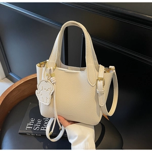 Detail of cream lychee leather tote with dual handles and puppy bag charm on a seat