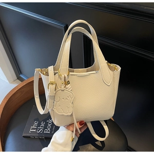 Detail of cream lychee grain leather bucket bag with dog charm and gold hardware