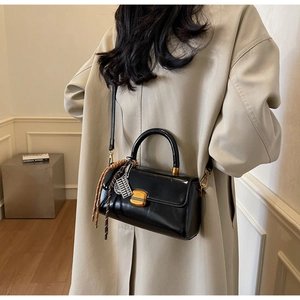 Detail of black glossy handbag with gold lock and decorative charms on a beige trench coat