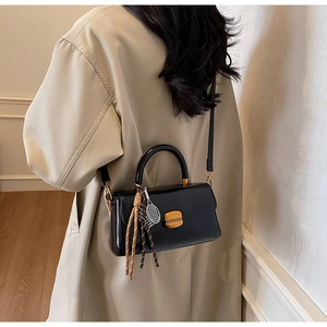 Detail of black leather crossbody bag with gold buckle and tennis racket charm accessory