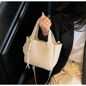 Detail of off-white lychee grain leather bucket bag with cute bear charm and gold hardware