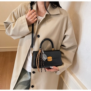 Detail of glossy black patent leather handbag with gold lock and metal tennis racket charm