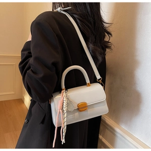 Detail of grey patent leather handbag with pink tassel and tennis racket charm accessory