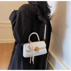 Detail of a chic leather shoulder bag featuring a gold buckle and knotted silk scarf
