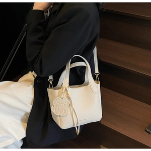 Detail of off-white leather bucket bag with puppy charm on wooden steps background