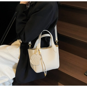 Detail of white lychee leather bucket bag with puppy charm and gold-tone hardware