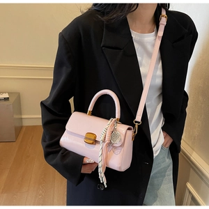 Detail of pink patent leather handbag with gold clasp, scarf knot, and tennis racket charm