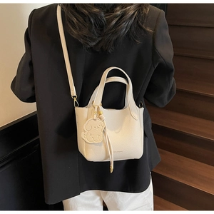 White lychee leather bucket bag with dog charm on person against a staircase
