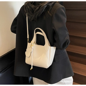 Model wearing a creamy white pebble leather bucket bag with dog charm and gold hardware