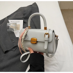 Detail of off-white faux leather handbag featuring golden lock and woven pendant charm