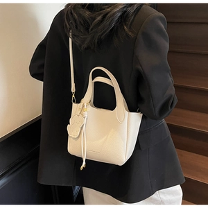 Creamy white lychee grain leather bucket bag with dog pendant worn over the shoulder