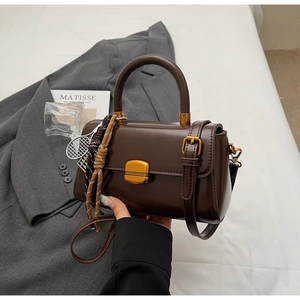 Detail of chocolate brown leather handbag featuring gold metal lock and tennis racket charm