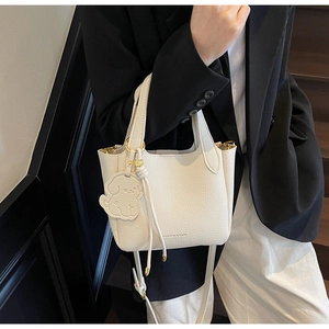 Close-up of white lychee leather bucket bag with cute dog pendant and shoulder strap