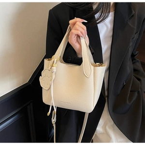 Detail of beige lychee grain leather bucket bag with cute dog charm and gold logo