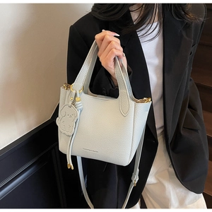 Detail of light blue bucket bag with pebble leather texture and cute dog charm