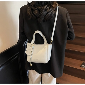 Close-up of white lychee pattern leather bucket bag with puppy charm and gold hardware
