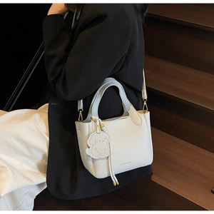 Detail of light blue pebbled leather bucket bag with cute dog charm and golden hardware