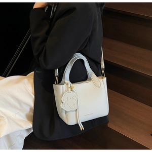 Detail of grey lychee leather bucket bag with puppy charm and gold hardware on stairs
