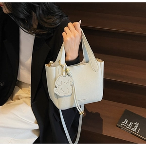 Detail of light lychee leather bucket bag with dog charm on wooden stairs