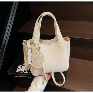 Close-up of litchi grain cream white leather bucket bag with dog-shaped charm detail