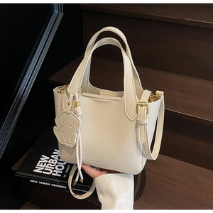 Detail of cream lychee leather bucket bag with gold hardware and dog-shaped charm