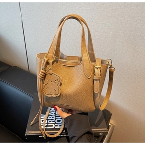 Detail of brown litchi pattern leather bucket bag with cute dog charm and gold hardware
