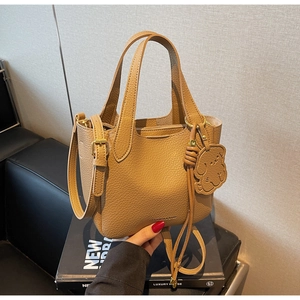 Close-up of brown litchi pattern bucket bag with cute dog pendant and adjustable strap