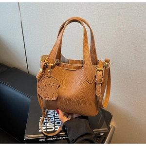 Close-up of brown litchi pattern bucket bag with dog charm and fashion embossing