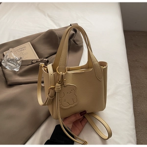 Detail of beige lychee leather bucket bag with cute bear charm and shoulder strap