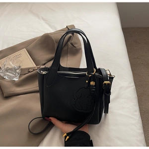 Detail of black litchi grain bucket bag with cute dog emblem and gold hardware