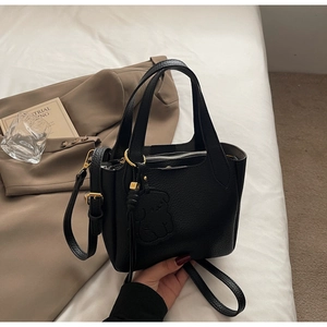 Close-up of black lychee texture leather bucket bag with gold hardware and bear charm