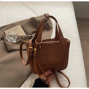 Close-up of caramel brown pebble leather bucket bag with gold hardware and dog charm
