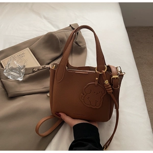 Detailed view of a brown pebbled leather bucket bag with a cute dog charm on a blazer