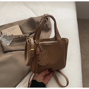 Close-up of brown litchi leather bucket bag with a cute bear charm and golden hardware
