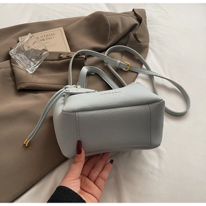Detail of light blue bucket bag with pebble leather texture and gold hardware on blazer