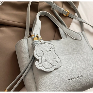 Macro shot of light blue lychee pattern leather bucket bag with cute dog charm and gold hardware