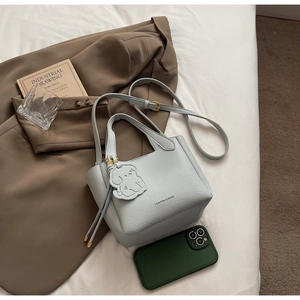 Detailed shot of litchi grain leather bucket bag with puppy charm on white fabric