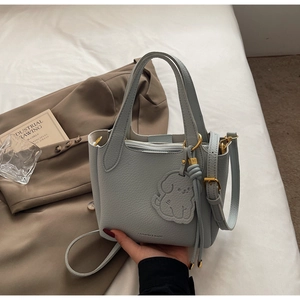 Close-up of light blue leather bucket bag with dog charm and gold hardware on white background