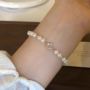 Detail of baroque pearl bracelet featuring a gold-rimmed four-leaf clover charm on wrist