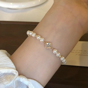 Detail of a pearl bracelet with gold clover charm worn on a female wrist
