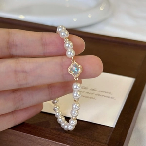 Macro detail of baroque pearl bracelet featuring a gold four-leaf clover pendant inlay