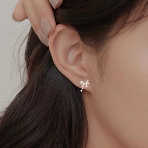 Close-up of elegant bowknot star earrings on ear lobe with delicate hanging chain detail